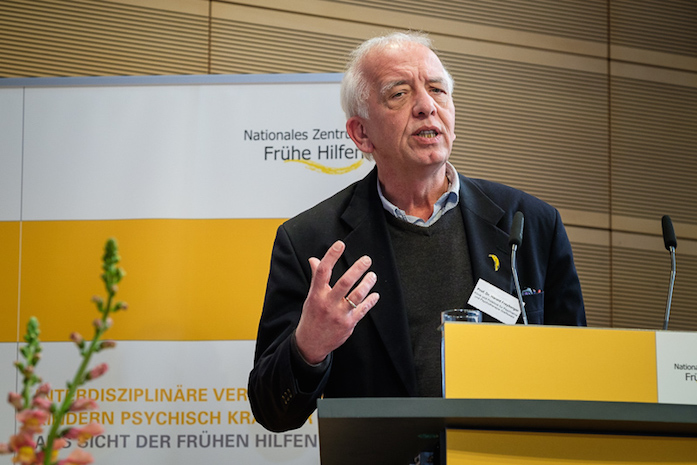 Prof. Dr. Harald Feyberger bei seinem Vortrag am Rednerpult, dahinter ein Plakataufsteller mit Logo des NZFH