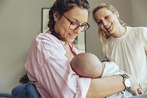 Eine Stillberaterin hilft einer jungen Mutter beim Anlegen ihres Babys.