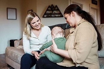 Eine Familienhebamme besucht eine Mutter mit Baby auf dem Schoß.