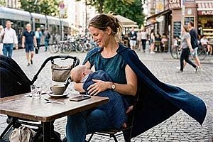 Stillende Frau sitzt mit Baby im Außencafé und trägt einen blauen Umhang