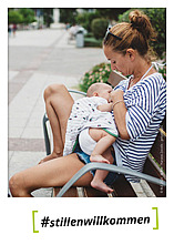 Postkartenmotiv #stillenwillkommen Postkarte mit Foto einer Frau die auf einer Parkbank ihr Baby stillt