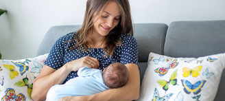 Mutter sitzt auf Sofa und stillt ihr Baby