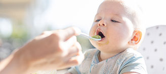 Baby in Hochstuhl wird mit Brei gefüttert