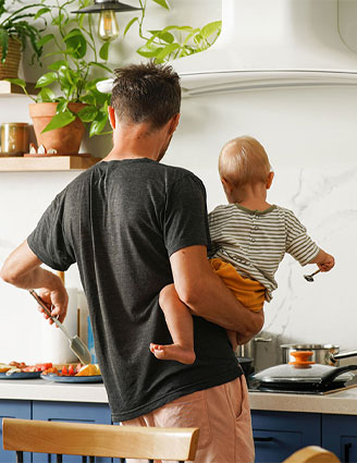 ein Vater trägt sein Baby auf dem Arm und kocht