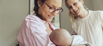Eine Stillberaterin hilft einer jungen Mutter beim Anlegen ihres Babys.