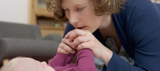Mutter wendet sich Baby zu und hält es an den Händen