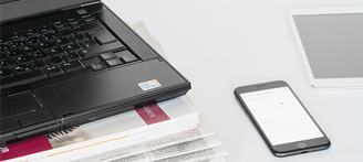 PC-Notbook auf Zeitungsstapel mit daneben liegendem Smartphone und Tablet