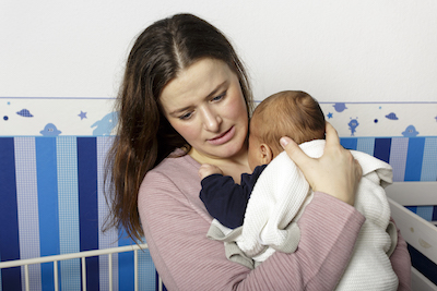 Gestresste Mutter hält schreiendes Baby im Arm an sich gedrückt