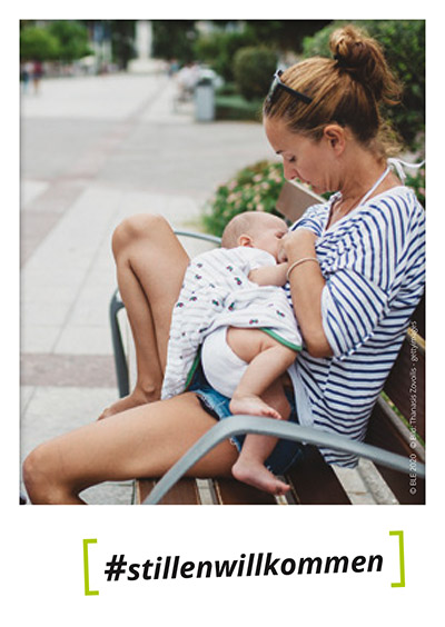 Postkartenmotiv #stillenwillkommen Postkarte mit Foto einer Frau die auf einer Parkbank ihr Baby stillt