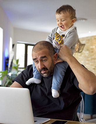 Mann mit Kind auf den Schultern vor einem Laptop