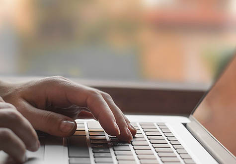 Ausschnitt zeigt Hände an Laptop Tastatur
