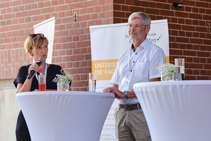 Yvonne Hoyer-Bachmann am Mikrofon spricht mit PD Dr. Burkhard Rodeck an einem Stehtisch auf dem Podium
