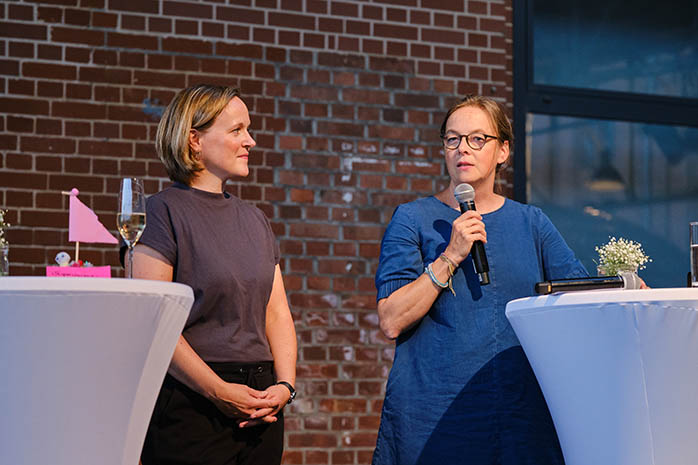 Almut Hornschild, am Mikrofon, und Julia Funk an Stehtischen auf dem Podium