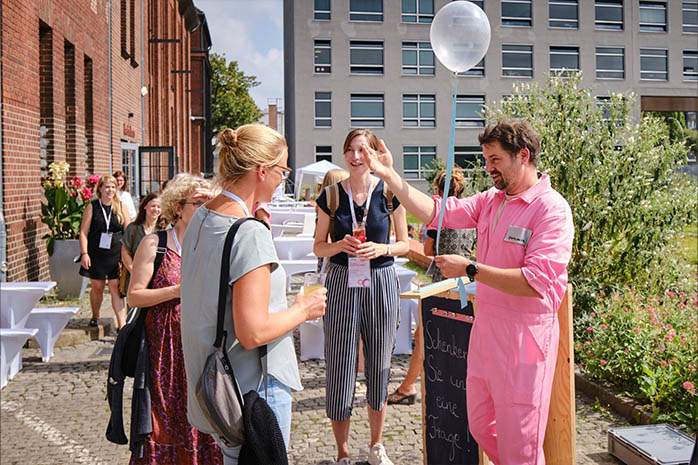 Ein Mitglied der Kompanie Kopfstand e.V. mit Ballon in der Hand im Gespräch mit Teilnehmenden