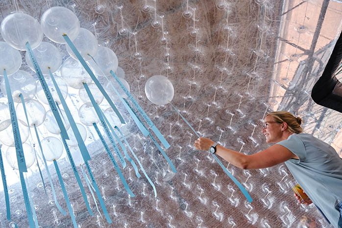 Teilnehmende lässt Ballon mit beschriftetem Band in eine transparente Kuppel zu weiteren Ballons aufsteigen