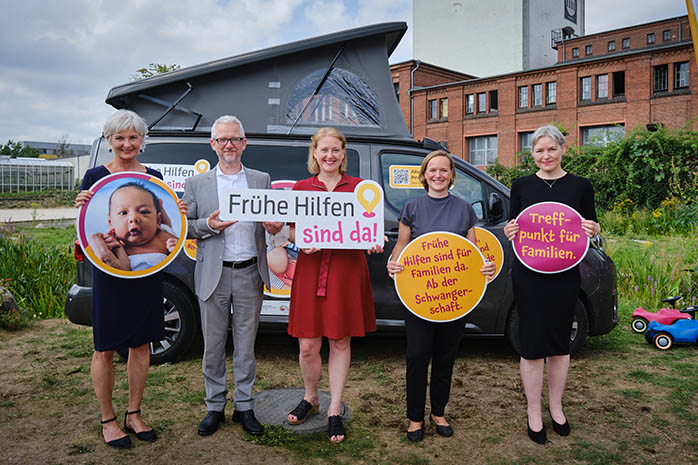 Lisa Paus, Mechthild Paul, Prof. Dr. Martin Dietrich, Julia Funk und Dr. Christina Boll stehen mit Schildern vor einem Frühe Hilfen Bus am Veranstaltungsort