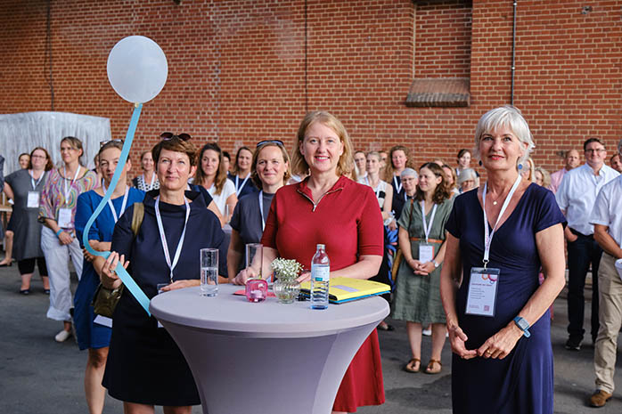 Lisa Paus, Bettina Bundzus, mit Ballon in der Hand, und Mechthild Paul an einem Stehtisch mit Teilnehmenden im Hintergrund