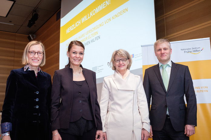 Gruppenbild mit Prof. Dr. Sabine Walper, Dr. Miriam Saati, Dr. med. Heidrun Thaiss und Dr. Thomas Stracke, hinter ihnen ein Plakataufsteller und eine Projektionswand mit Begrüßung der Teilnehmenden