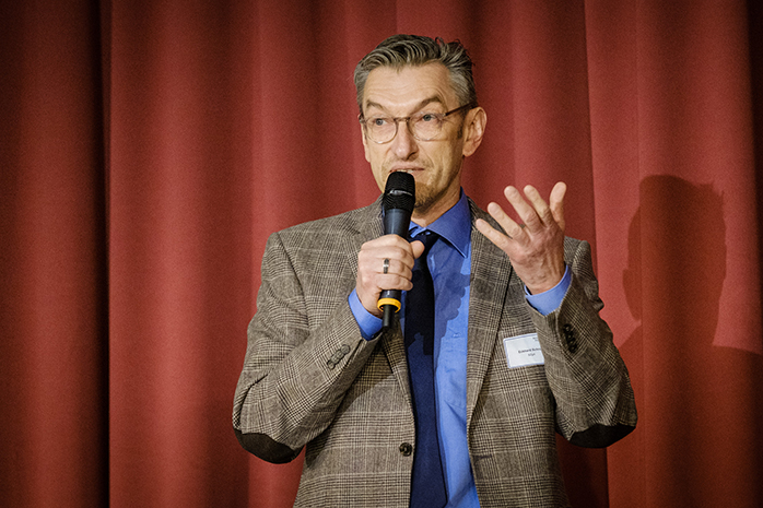 Eckhard Schroll spricht in ein Mikrofon, dahinter ein roter Vorhang
