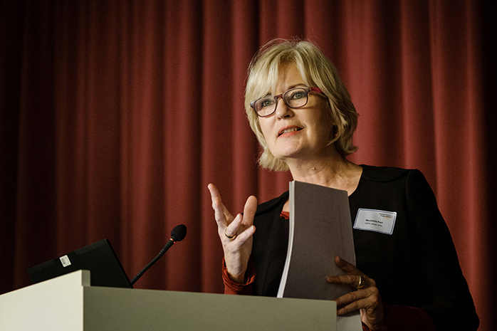 Mechthild Paul bei ihrem Vortrag am Rednerpult, dahinter ein roter Vorhang