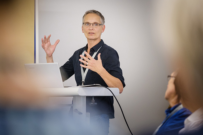 Pia Peddinghaus steht an einem Rednerpult mit Laptop, sie gestekuliert mit den Händen