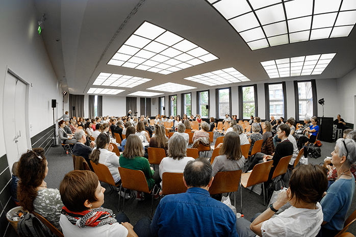 Teilnehmende sitzen in einem Stuhlkreis mit mehreren Reihen