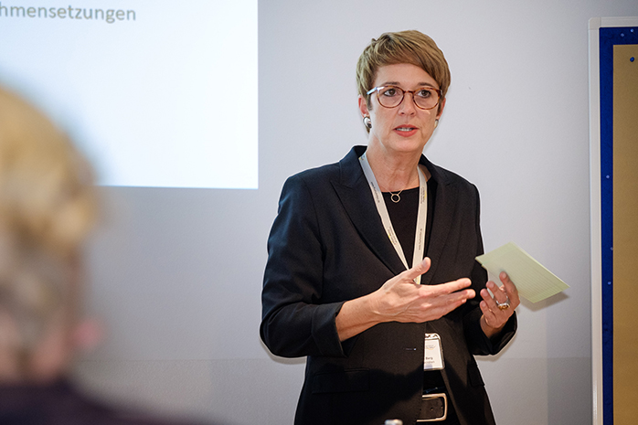 Stadträtin Annette Berg steht vor Projektionswand und gestekuliert mit Zettel in der Hand