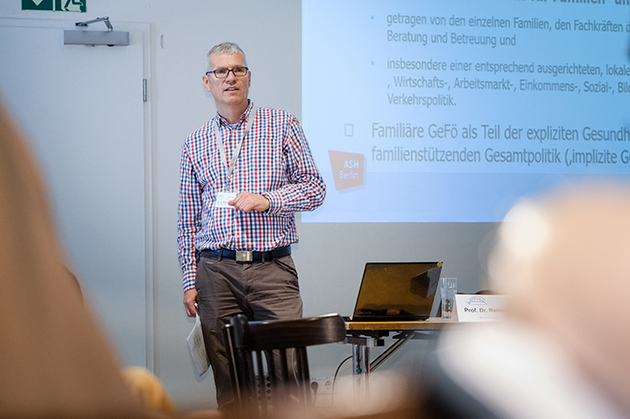 Prof. Dr. Raimund Geene vor Leinwand stehend