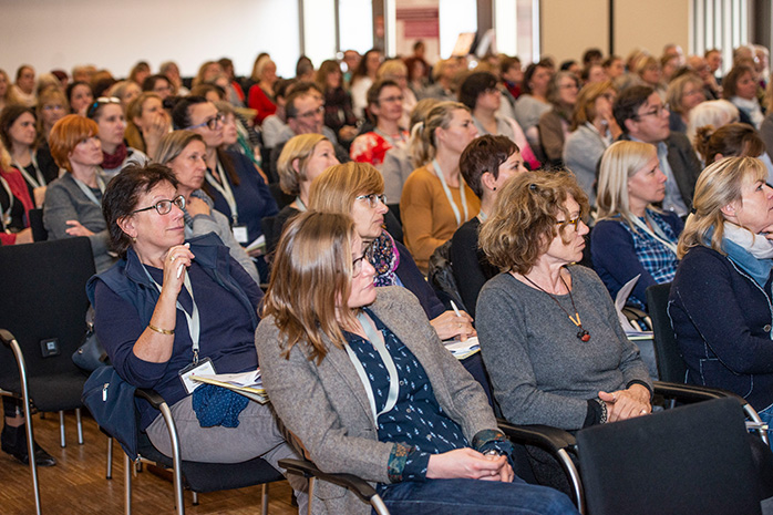 Konferenzteilnehmende auf Stühlen sitzend