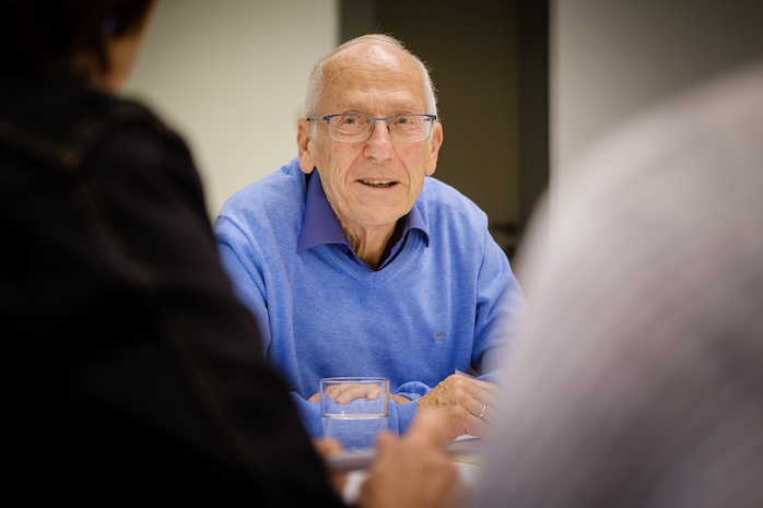 Ein älterer Mann mit Brille sitzt an einem Thementisch.