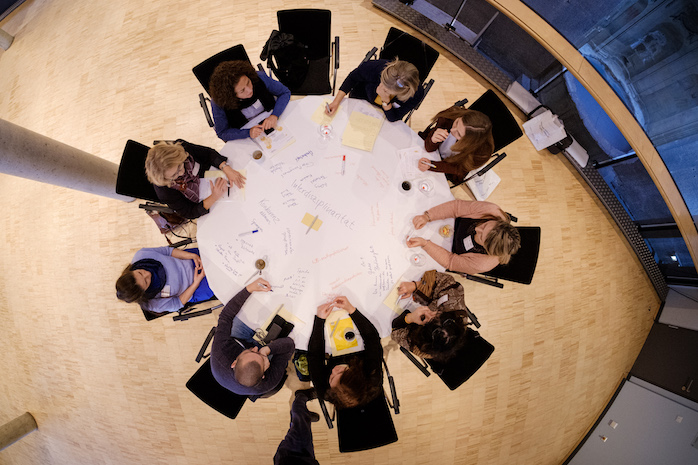 Perspektive von oben auf einen Themen-Tisch mit Teilnehmerinnen und Teilnehmern