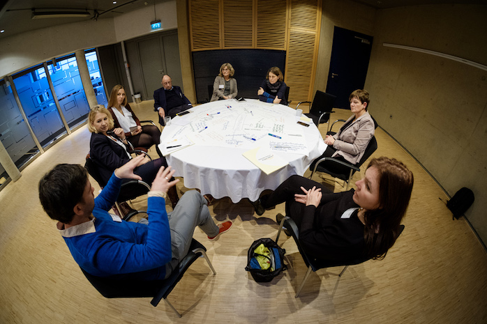 Teilnehmerinnen und Teilnehmer sitzen um einen runden Tisch