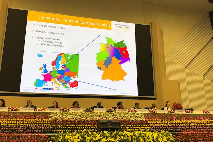 Vortragende sitzen vor großer Leinwand mit eingeblendeter Grafik